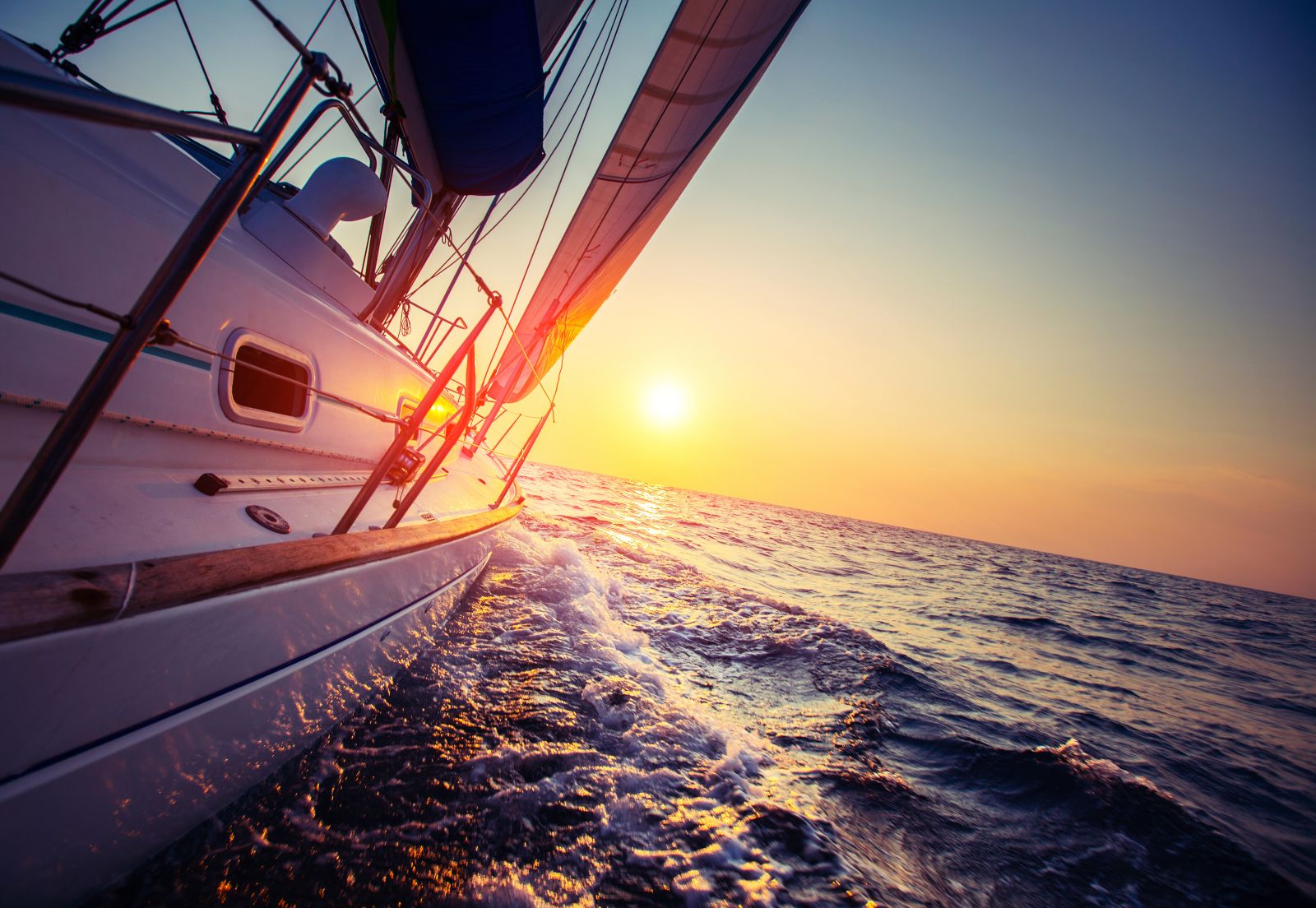 Sail boat with set up sails gliding in open sea at sunset