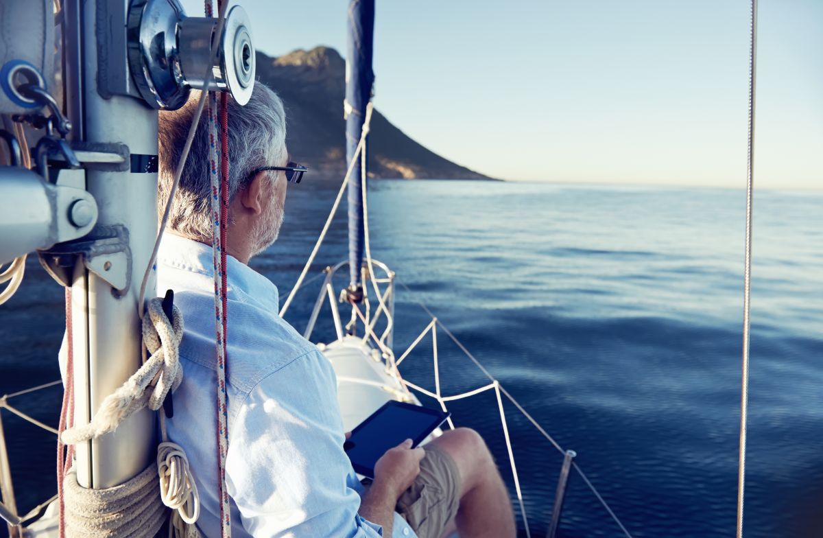 sailing man reading tablet computer on boat with modern technology and carefree retired senior successful lifestyle